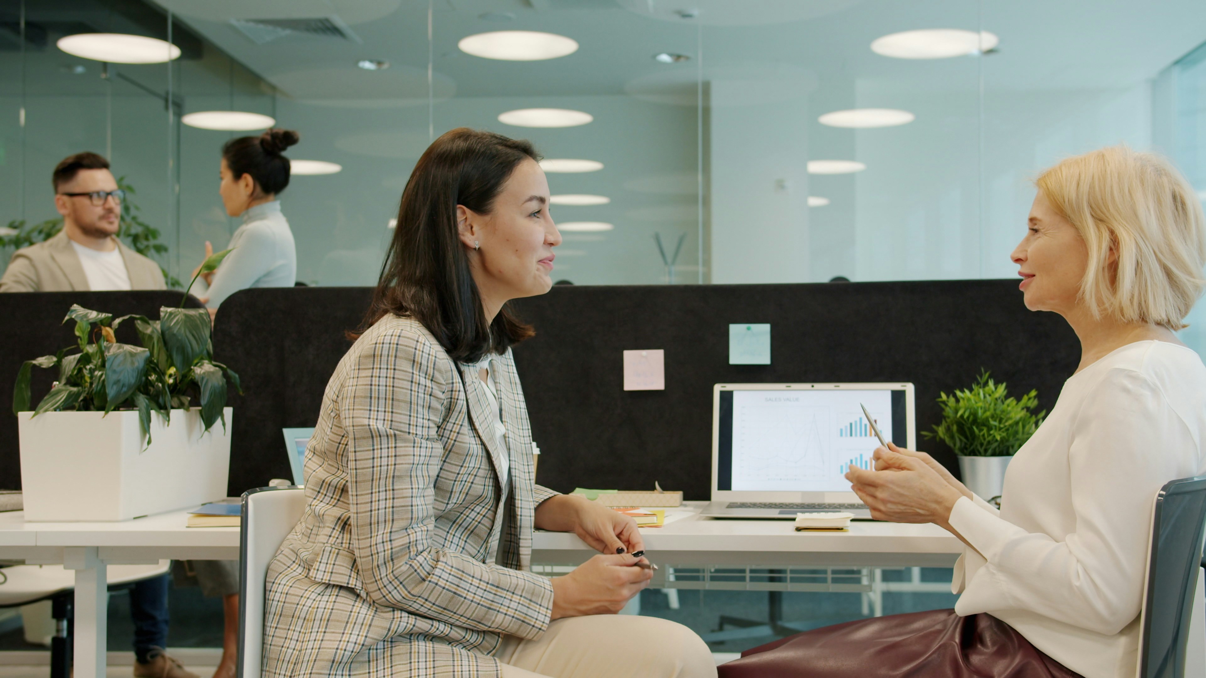 Two colleagues talking across a desk in a bright open-plan office